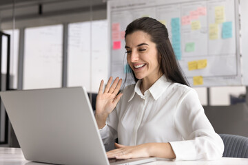 Smiling Hispanic businesswoman greeting client or colleague starting videoconference call seated in...