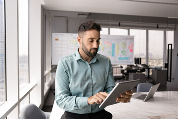 Young 30s Hispanic man engaged in work-related workflow, reading reports, business documents,...