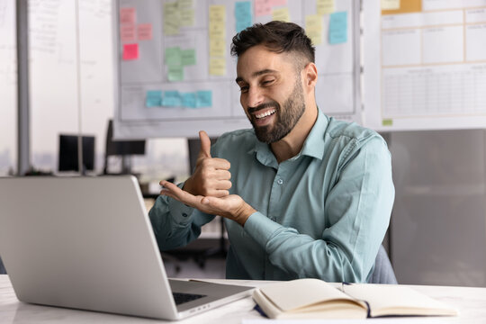 Latino man sits at desk, take part in videocall use application, showing hand gesture during digital communication in office, give positive feedback with thumbs-up sign. Business virtual meeting event