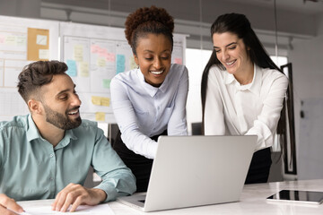 Multiracial teammates collaborate on project presentation using laptop, review performance metrics,...
