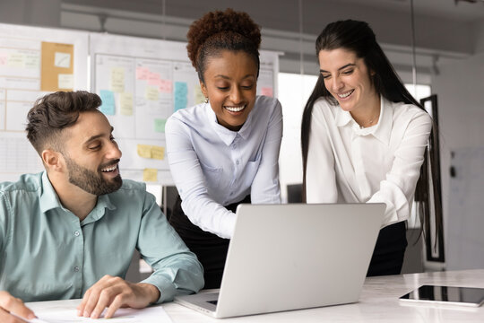 Multiracial teammates collaborate on project presentation using laptop, review performance metrics, discuss new marketing strategy, smiling, feel satisfied with productive, effective teamwork results - Powered by Adobe