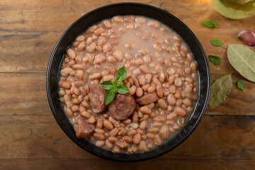Brazilian beans with sausage in a black bowl on a rustic wooden background