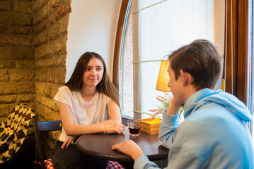 Teenagers, a girl and a boy, are sitting in a cafe, waiting for an order.