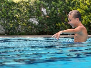 A joyful boy standing waist-deep in a swimming pool, bursting with emotion — either laughing or...