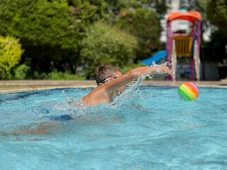 A boy is playing with a ball in a swimming pool. Summer activity, fun in water, childhood joy,...