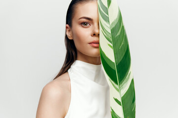 Young woman holding a large green leaf, showcasing a natural and serene beauty in a minimalistic...