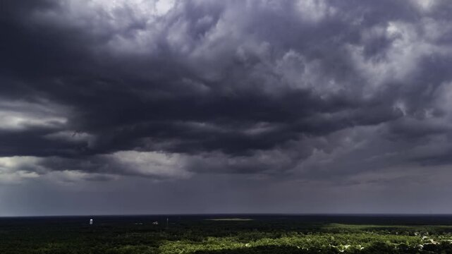 Aerial time-lapse captured by a drone, showcasing a dramatic storm front rolling over a dense, green wooded landscape.