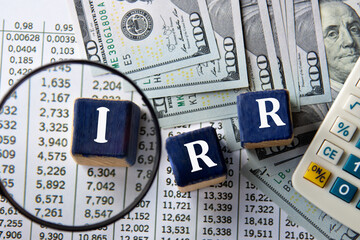 IRR - acronym on wooden cubes against the background of banknotes and calculator