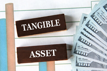 TANGIBLE ASSET - words on brown wooden blocks on the background of a graph and banknotes