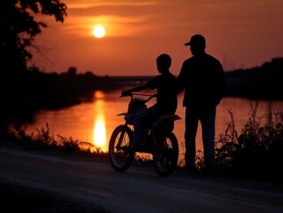 Obraz premium Silhouette of a man and boy with a dirt bike by a river at sunset