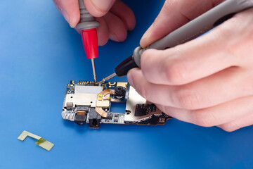 Person repairing a smartphone circuit board using test probes on a blue surface in a close up shot