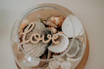 Une décoration en bois avec le mot "love" dans un bocal avec des coquillages 