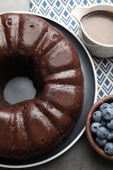 Tasty chocolate bundt cake and blueberries on grey table, top view