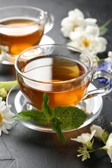 Aromatic herbal tea in glass cups, different flowers and mint on black table, closeup
