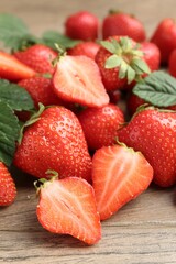 Delicious ripe strawberries and green leaves on wooden table, closeup