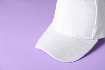 White baseball hat on violet background, closeup. Space for text