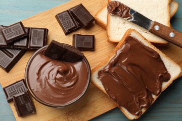 Tasty chocolate butter, pieces, knife and slices of bread on light blue wooden table, top view