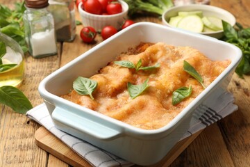 Tasty vegetarian lasagna in baking dish and ingredients on wooden table, closeup