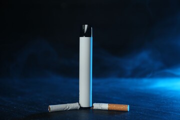 Electronic smoking device and broken cigarette on black table in blue light