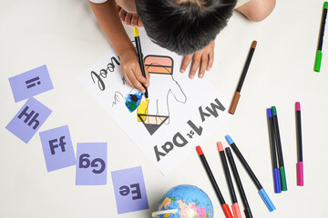Top view of a child coloring a first day of school worksheet, surrounded by colorful markers,...