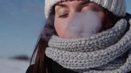 woman exhaling visible breath in the cold winter air, bundled up against the low temperatures