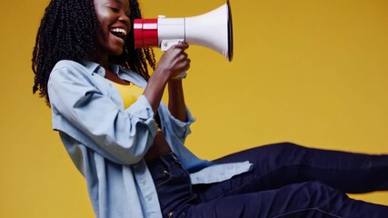 Energetic young woman holding megaphone and making an announcement in bright yellow studio - Powered by Adobe