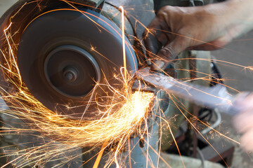 Worker working with hand grinder on metal construction. Electric wheel grinding on steel structure in factory. Knife sharpening