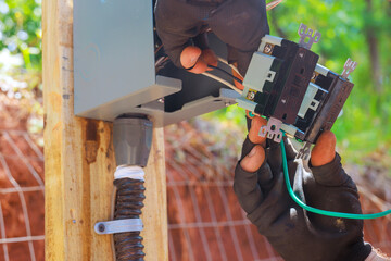 An electrician works on wiring circuit breaker in an outdoor electrical panel to outlets connecting wires