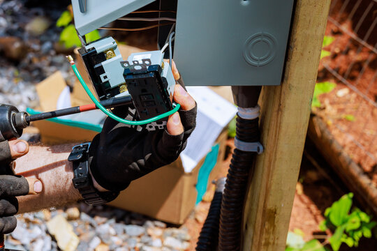 An electrician connects wires to new electrical panel in an outdoor setting, to outlets on safety precision.