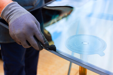 Technician carefully coats edge of windshield with adhesive while preparing to replacement windshield