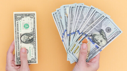 Hands holding one dollar bill and a fan of hundred dollar bills against a vibrant orange...
