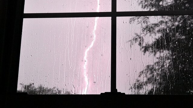 Lightning strike illuminating a stormy sky through a rain-streaked window
