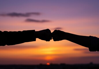 Fist bump silhouette at sunset symbolizes collaboration and success.