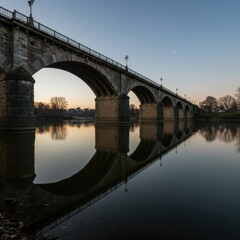 Fototapeta premium Stunning Evening Reflection of a Majestic Stone Arch Bridge Over a Serene River at Dusk