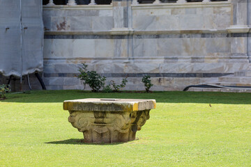 A stone sarcophagus or part of a funerary monument within the cemetery's central grassy courtyard of the Camposanto Monumentale (Monumental Cemetery) in Pisa, Italy.