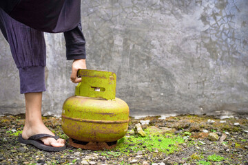 A hijab-wearing woman's hand carries a heavy gas cylinder outdoors, showing a scene of manual...