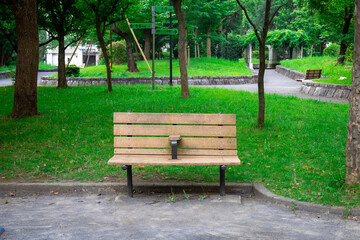 Empty wooden bench in a serene public park, surrounded by vibrant green grass and trees. 