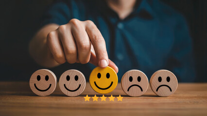 Hand selecting happy face with five star rating on wooden table