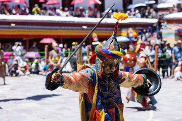 A masked performer in vibrant costume wields a sword and shield during a dramatic Cham dance at the Hemis Festival in Ladakh. This ritual showcases Tibetan Buddhist culture and ceremonial artistry.