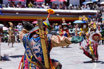 A masked performer in vibrant costume wields a sword and shield during a dramatic Cham dance at the...