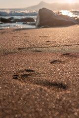 Footprints in golden sand leading to the ocean at sunset. Ideal background for travel, lifestyle, or wellness product placement in calm, natural beach settings.