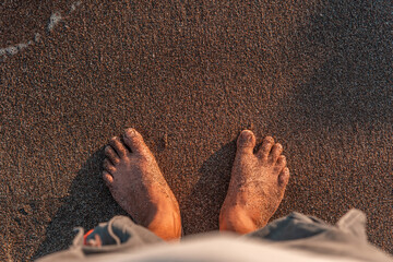 POV of bare feet standing on a wet sandy beach at sunset. Peaceful moment of relaxation, travel, and mindfulness captured in golden hour lighting.