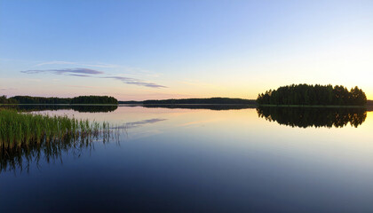 Obraz premium Serene lake panorama calm water sunrise reflection forest island tranquil landscape peaceful nature scene smooth water surface early morning light blue sky green reeds water reflection natural