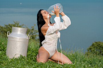 Female model with dripping milk on sexy body. Woman drink milk from bottle near Swiss Alps. Woman...