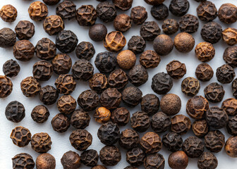 Obraz premium Black Peppercorns: A close-up shot shows an array of black peppercorns, each a tiny globe of flavor, scattered. The texture of each peppercorn offers a rich display of the versatility in food.