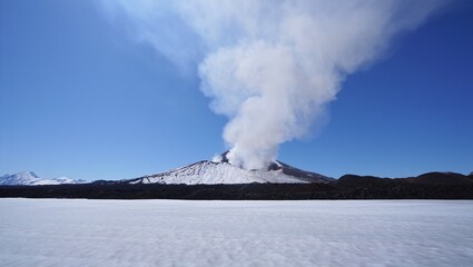 Fototapeta premium Snow covered volcano erupting with a plume of smoke against a blue sky