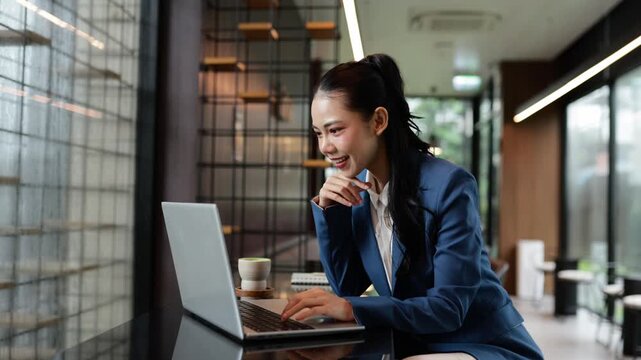 Professional Asian businesswoman working efficiently on laptop while enjoying matcha tea at modern office desk, focusing on project with concentration and strategic mindset