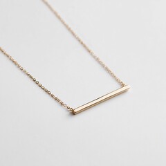 A close up shot of a delicate gold bar necklace resting on a clean white surface with soft lighting