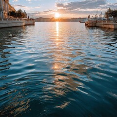 Scenic view of a riverside promenade during sunset with calm water reflections, historic buildings, boats docked along the waterfront, and a vibrant sky with clouds illuminated by the setting sun