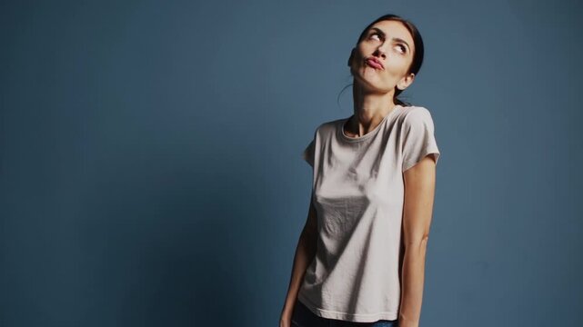 Close-Up Portrait of Playful Woman Making Suspicious Grimace While Looking Up on Blue Studio Background